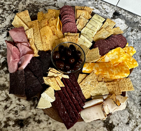 charcuterie board with bison elk ham chicken cheese crackers olives